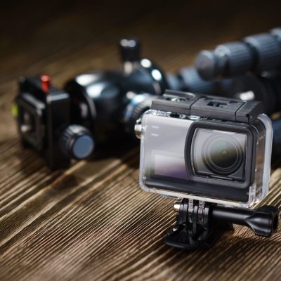 Black small action camera in waterproof housing and tripod on brown wooden tabletop.