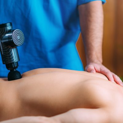Lower back treatment with massage gun. Physical therapist massaging man’s lower back