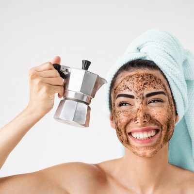 Young smiling woman applying coffee scrub mask on face - Happy girl having healthy skin care spa day at home - Alternative natural exfoliation treatment and people lifestyle concept