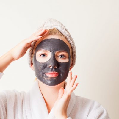 Woman using a black face mask, close up face with hands. Spa treatment
