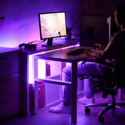 Gamer sitting at the table in front of computer monitor and playing computer game in dark room at home