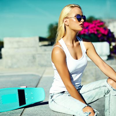 High fashion look.glamor stylish sexy beautiful young blond  model girl in summer bright casual hipster clothes with skateboard behind blue sky in the street