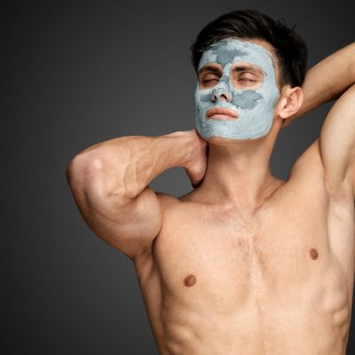 Portrait of a beautiful relaxed young man with a facial mud clay mask, face and body skin care treatment.