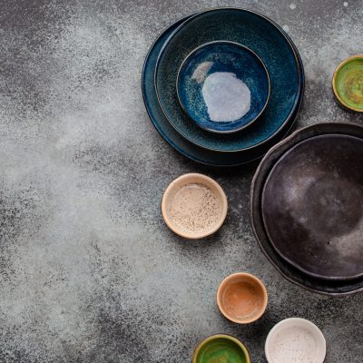 Assorted ceramic hand-made multicolored empty plates and bowls on rustic gray concrete background. Rustic table setting, set of plates. Top view of beautiful empty plates and bowls with space for text