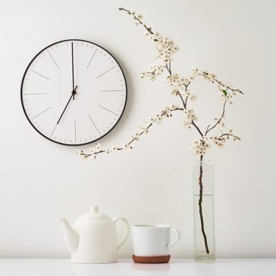 Wall clock, blooming cherry branch and tea cup on white background, front view. Interior decoration. Tea time
