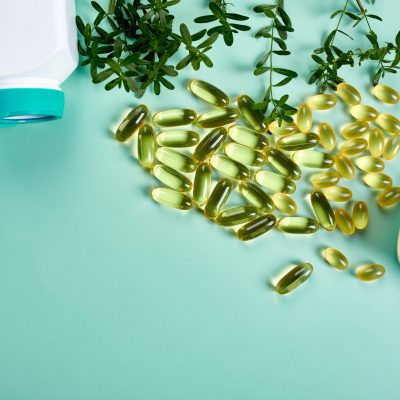 Capsules with fish oil and green leaves on green background, Healthcare concept, healthy food, Top view, copy space.